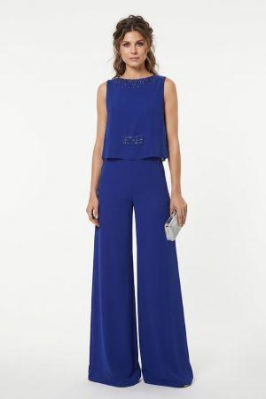 Mujer luciendo un elegante mono largo de fiesta azul eléctrico con pernera ancha y pedrería de frente.