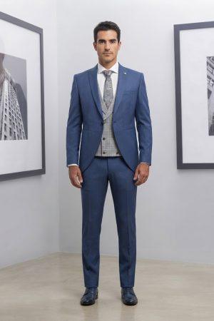 Novio luciendo un elegante traje azul con chaleco de cuadros y corbata estampada en un entorno de galería.