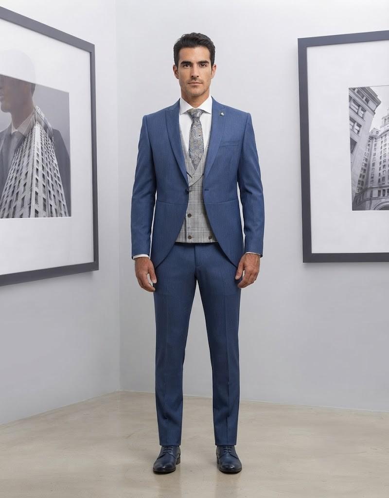 Novio luciendo un elegante traje azul con chaleco de cuadros y corbata estampada en un entorno de galería.