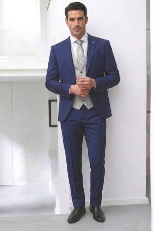 Novio o padrino con traje azul de dos botones, chaleco gris claro y corbata elegante.