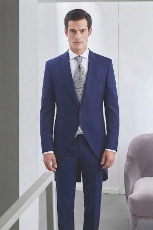 Novio luciendo un elegante chaqué azul moderno con corbata estampada y chaleco gris.