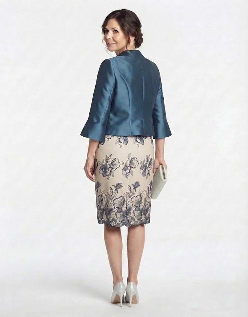 Modelo luciendo el conjunto midi con bordados florales y chaqueta bolero azul petróleo a juego.