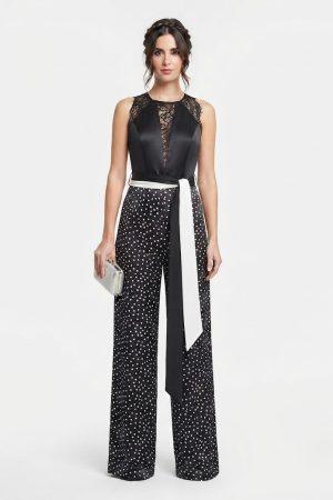 Mujer luciendo un elegante mono largo de fiesta negro de lunares con cuerpo de encaje de frente.