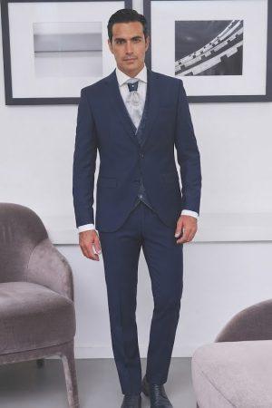 Hombre luciendo un traje azul marino elegante para novio y padrino con corbata y chaleco.