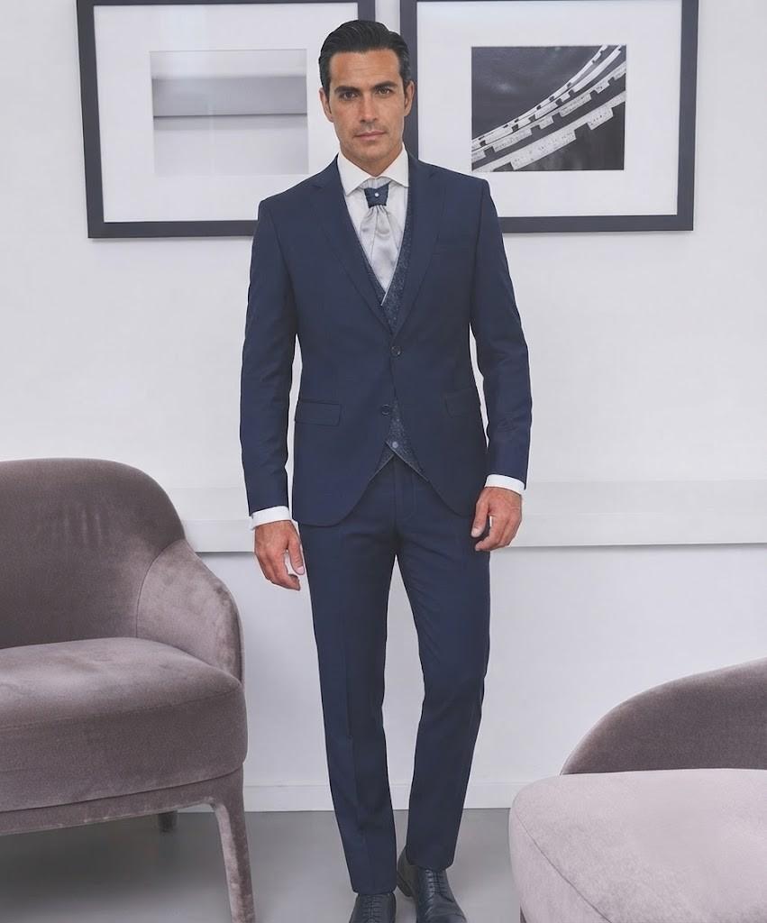Hombre luciendo un traje azul marino elegante para novio y padrino con corbata y chaleco.
