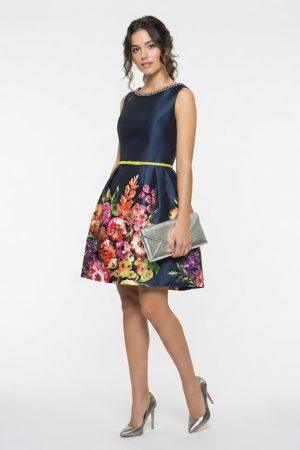 Modelo joven vistiendo vestido corto azul marino con flores y cartera plateada de fiesta.