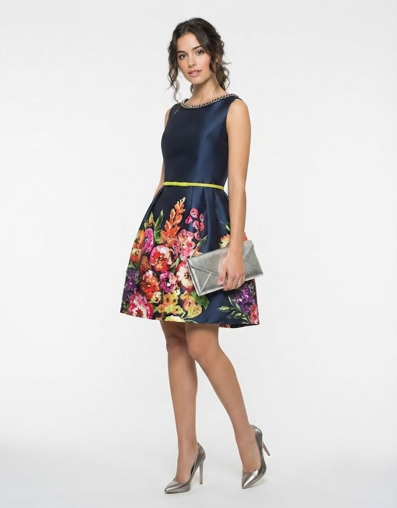 Modelo joven vistiendo vestido corto azul marino con flores y cartera plateada de fiesta.