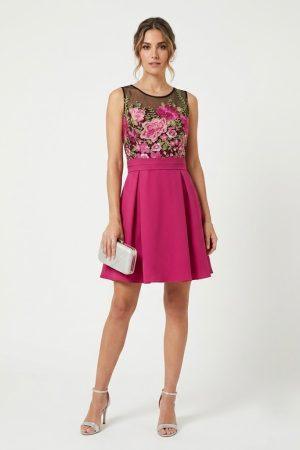 Modelo vistiendo un diseño corto de color fucsia con cuerpo de flores bordadas y falda con vuelo.