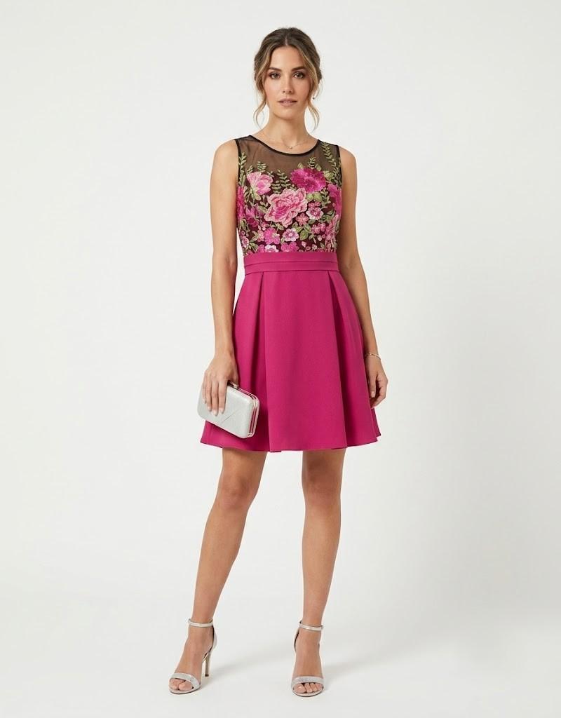 Modelo vistiendo un diseño corto de color fucsia con cuerpo de flores bordadas y falda con vuelo.