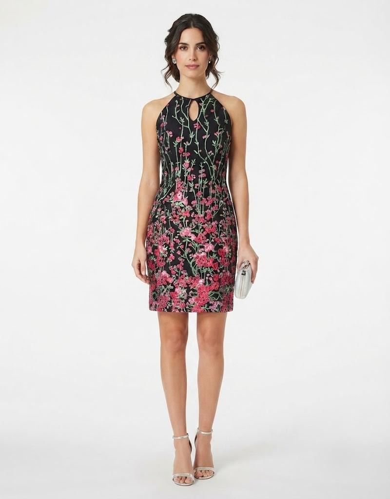 Modelo posando de frente con un diseño corto de fondo negro con estampado floral y escote halter con apertura.