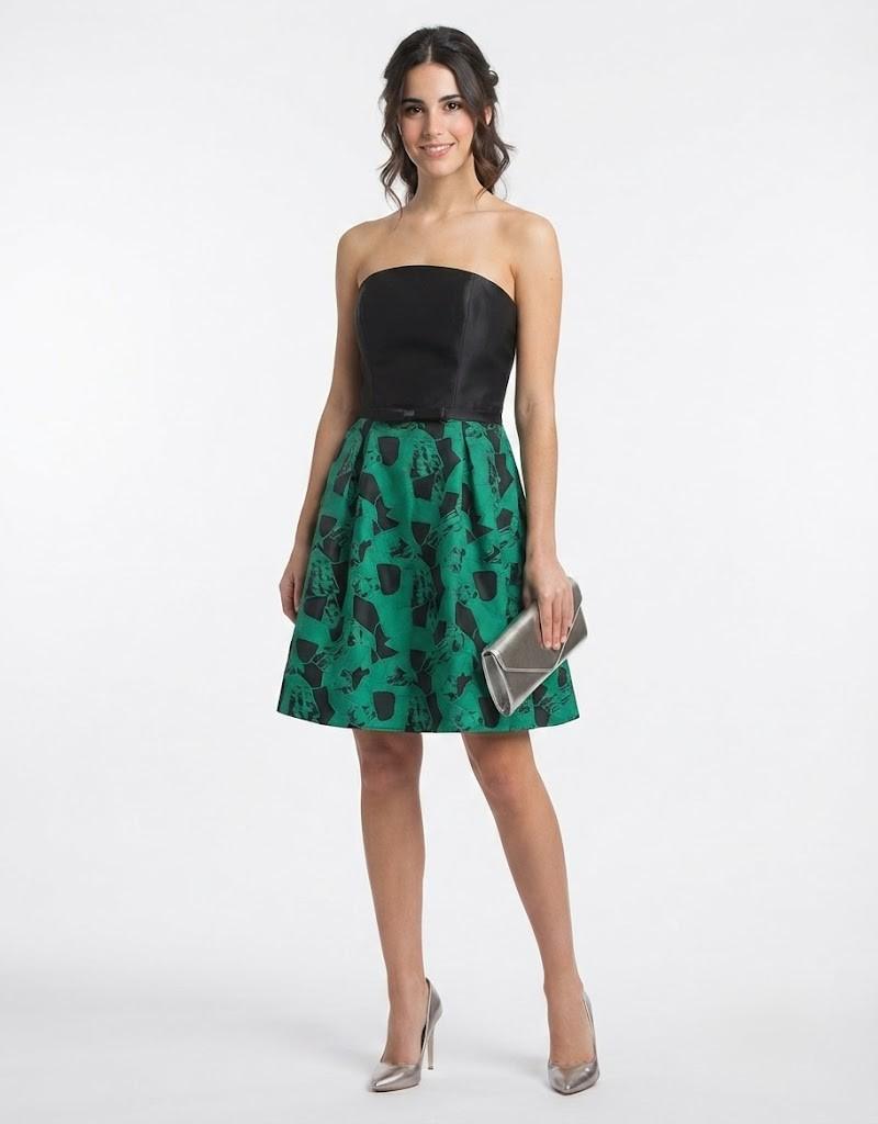 Modelo luciendo un elegante vestido corto negro y verde de ceremonia con escote palabra de honor.