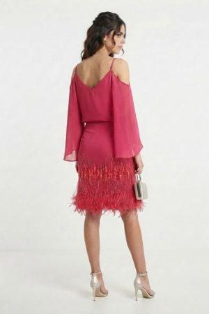 Modelo luciendo vestido corto de fiesta color fucsia con detalles de pedrería y plumas en el bajo