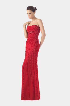 Vista frontal de modelo luciendo un vestido largo rojo de fiesta con escote palabra de honor y volantes texturizados.