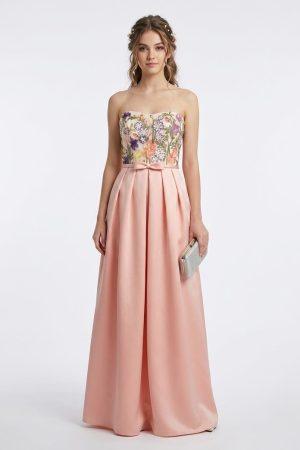 Mujer luciendo un elegante vestido largo de fiesta salmón con cuerpo bordado de flores y lazo en la cintura de frente.