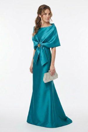 Mujer luciendo un elegante vestido largo de fiesta verde turquesa acompañado de una estola con broche joya
