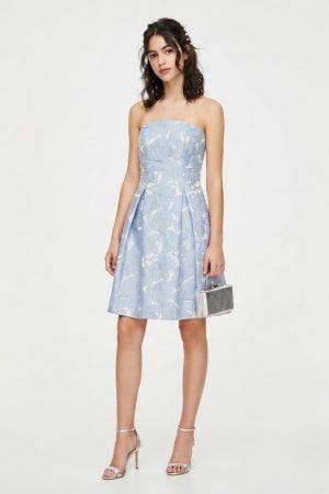 Modelo posando de frente con vestido corto azul palabra de honor y tejido jacquard floral.