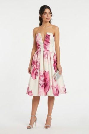 Mujer vistiendo vestido corto de fiesta con estampado floral y escote palabra de honor con abertura en V.