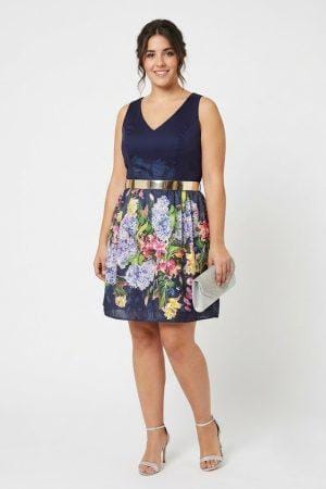 Modelo luciendo un vestido de fiesta corto con falda estampada floral y cinturón dorado.