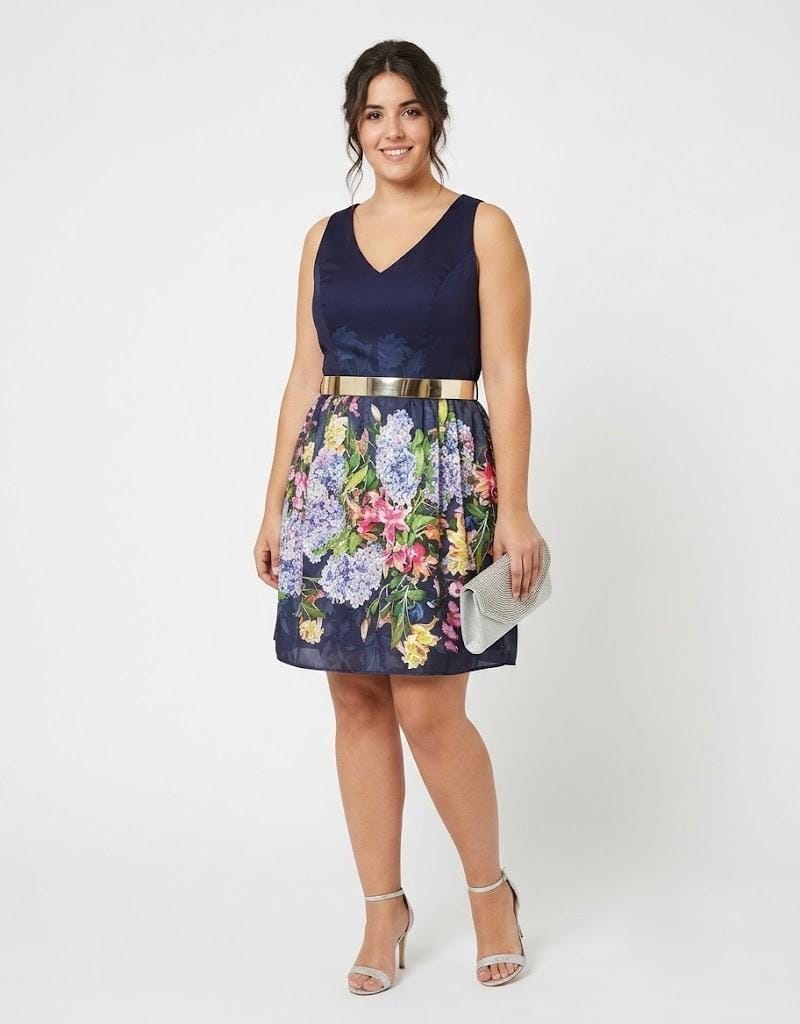 Modelo luciendo un vestido de fiesta corto con falda estampada floral y cinturón dorado.