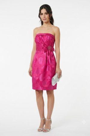 Mujer vistiendo vestido corto de fiesta color fucsia con escote palabra de honor y detalle floral en la cintura.