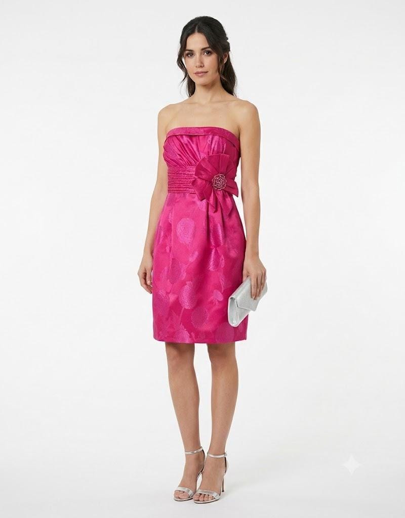Mujer vistiendo vestido corto de fiesta color fucsia con escote palabra de honor y detalle floral en la cintura.
