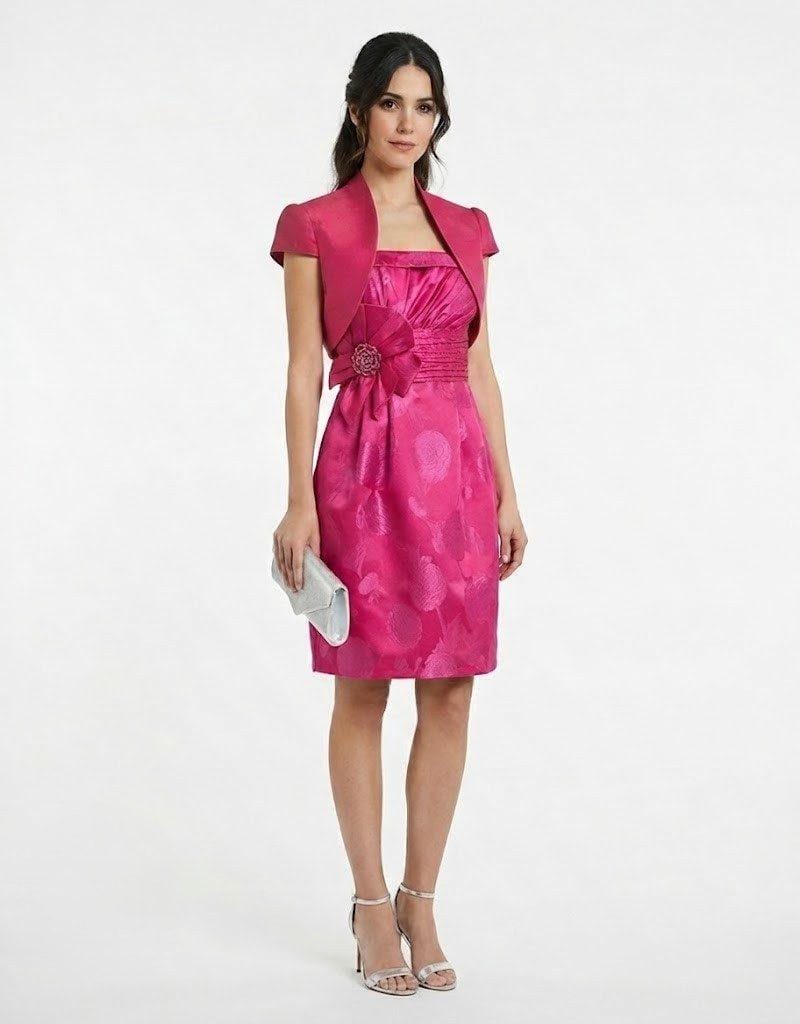 Mujer vistiendo vestido corto de fiesta color fucsia con escote palabra de honor, torera y detalle floral en la cintura.