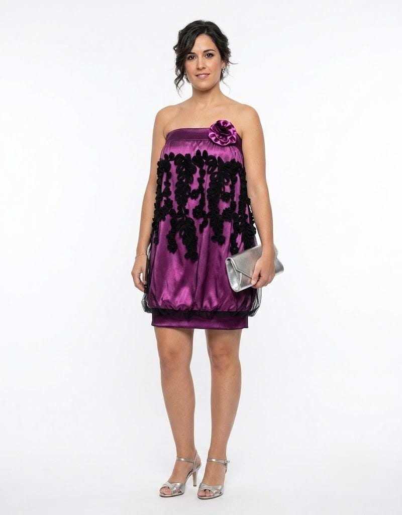 Modelo vistiendo un vestido de fiesta corto morado con corte tipo globo y detalles de flores negras en relieve.