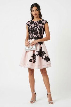 Mujer vistiendo vestido corto de fiesta color rosa con detalles de encaje floral negro.